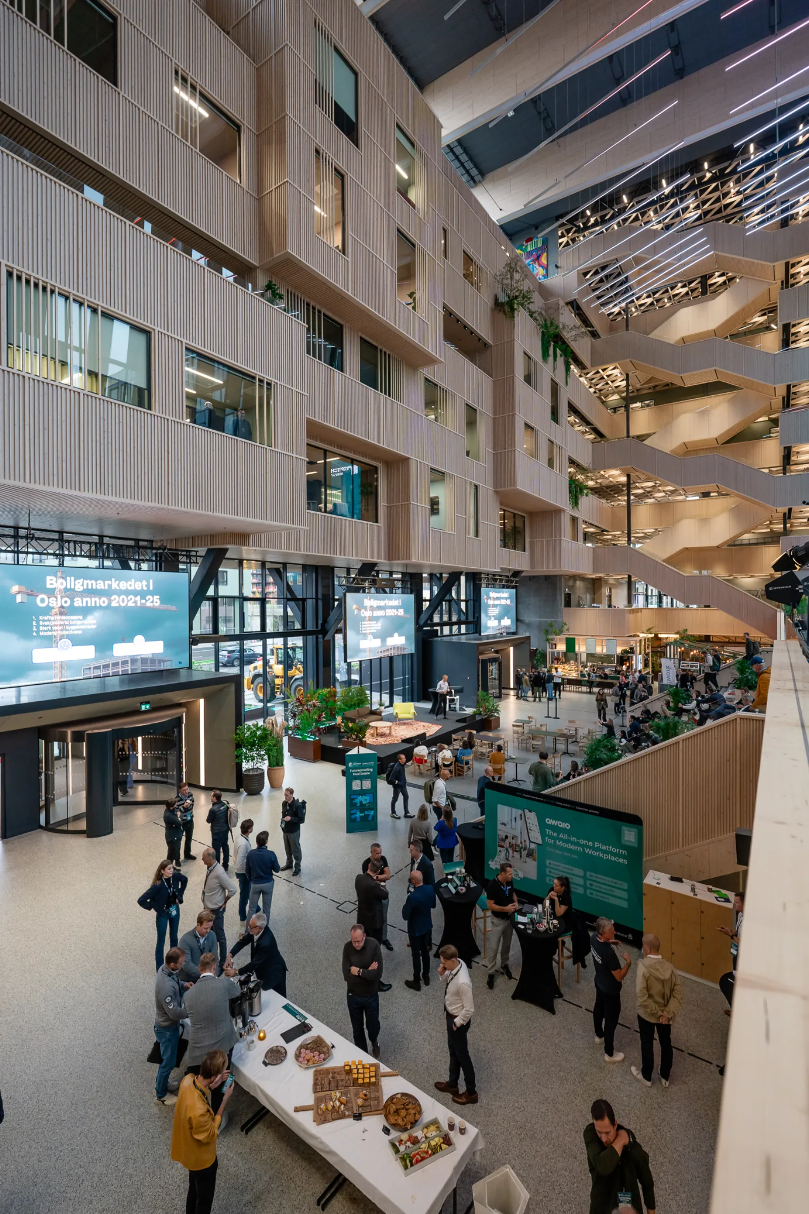 Attendees in the Construction City atrium at Oslo Proptech Summit 2025, with the Awaio screen visible